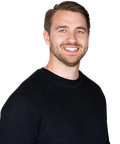 Smiling man with short hair and a beard wearing a black sweater against a plain background.