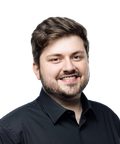 Smiling man with short brown hair and a beard, wearing a black collared shirt, against a white background.