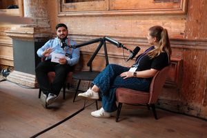 Two speakers recording a podcast-style interview during JoyConf, sitting across from each other in armchairs with microphones in a cozy wooden room.