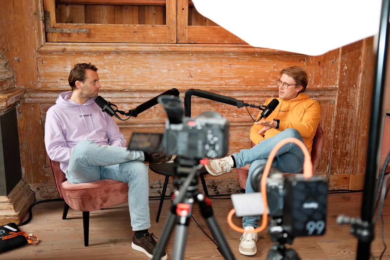 Two speakers recording a podcast-style interview during JoyConf, sitting across from each other in armchairs with microphones in a cozy wooden room.