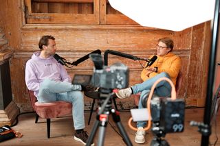 Two speakers recording a podcast-style interview during JoyConf, sitting across from each other in armchairs with microphones in a cozy wooden room.