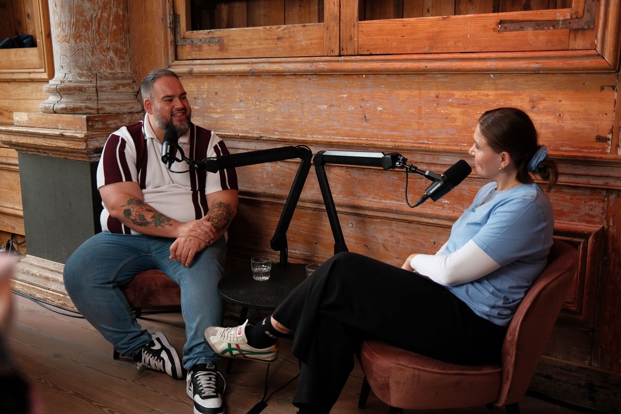 Two speakers recording a podcast-style interview during JoyConf, sitting across from each other in armchairs with microphones in a cozy wooden room.