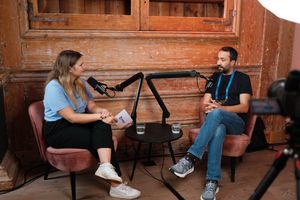 Two speakers recording a podcast-style interview during JoyConf, sitting across from each other in armchairs with microphones in a cozy wooden room.