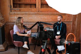 Two speakers recording a podcast-style interview during JoyConf, sitting across from each other in armchairs with microphones in a cozy wooden room.