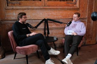 Two speakers recording a podcast-style interview during JoyConf, sitting across from each other in armchairs with microphones in a cozy wooden room.