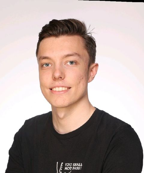 Smiling person with short dark hair wearing a black shirt, standing against a plain white background.