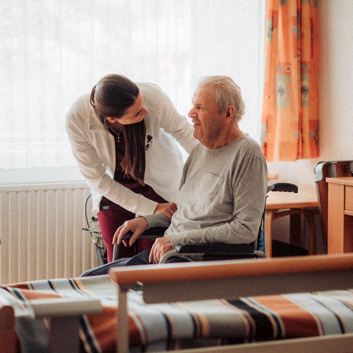 Eine Sozialbetreuerin hält die Hand eines Bewohners und unterhält sich zugewandt mit ihm.