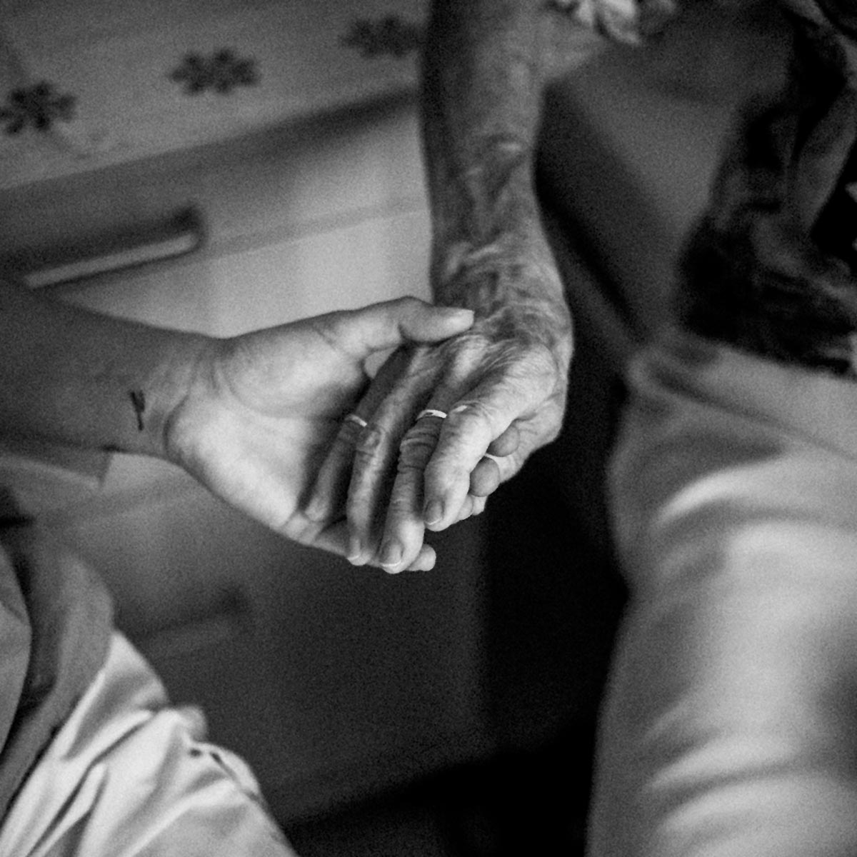 Eine Pflegeperson hält liebevoll die Hand einer älteren Dame.