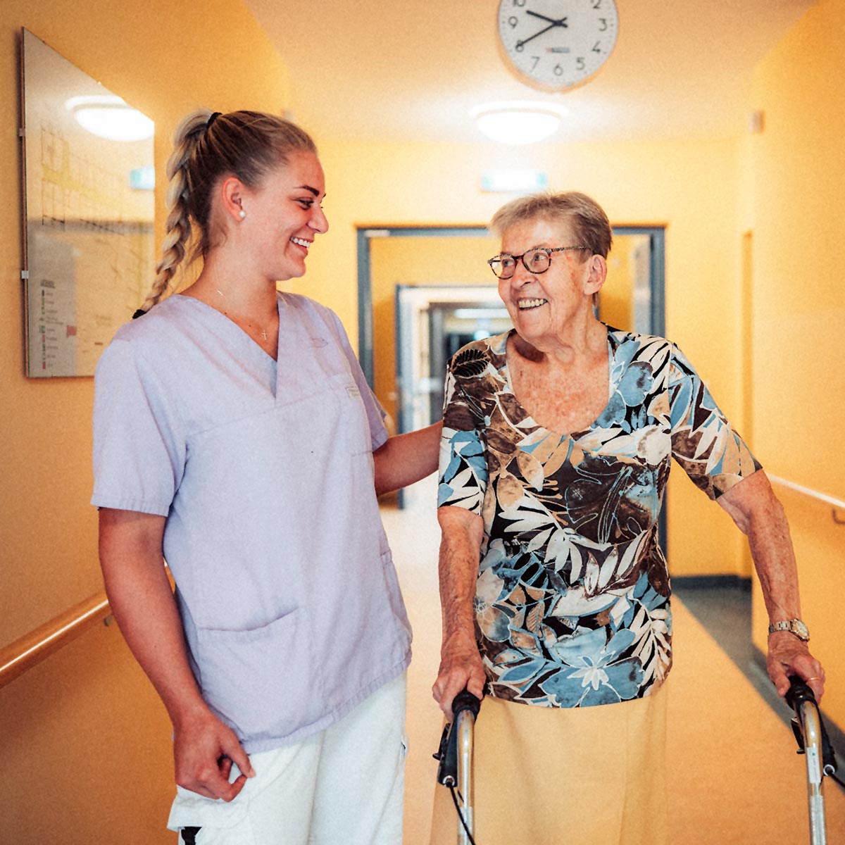 Eine junge Pflegekraft unterstützt eine Bewohnerin beim Gehen mit Rollator