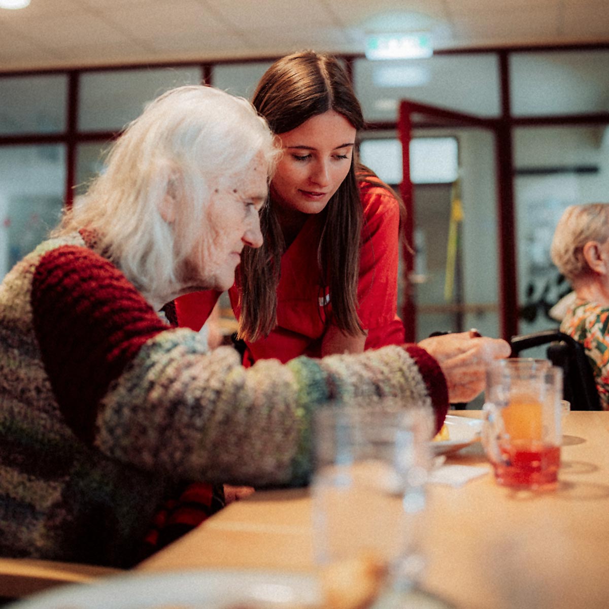 Ein Pflegelehrling unterstützt eine ältere Bewohnerin beim Essen.