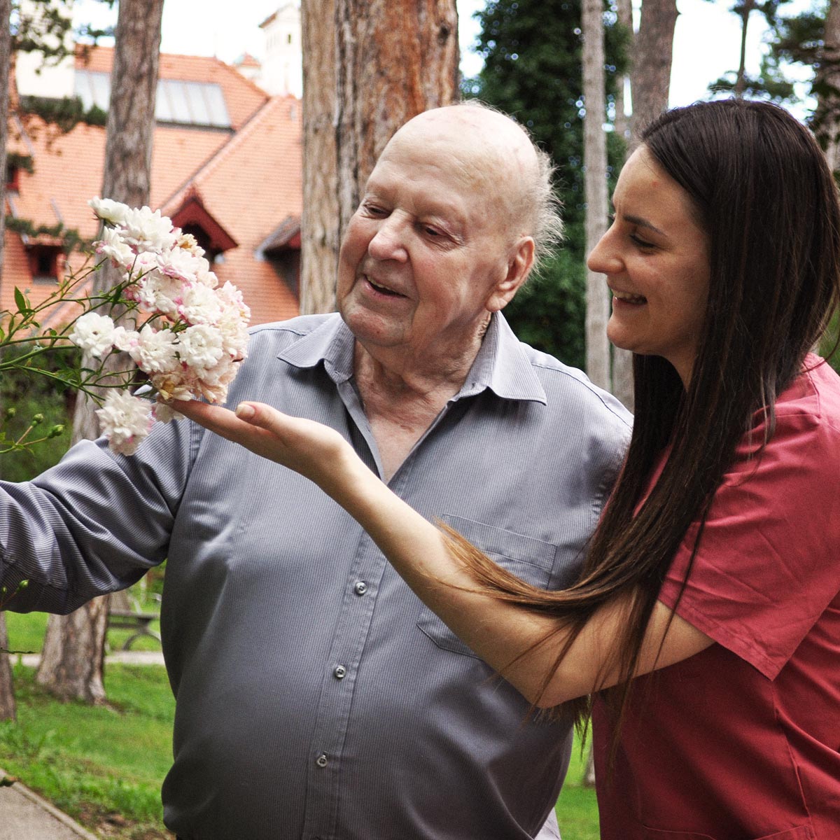 Ein Bewohner bewundert die duftenden Rosen im Garten, zusammen mit der Sozialbetreuerin.