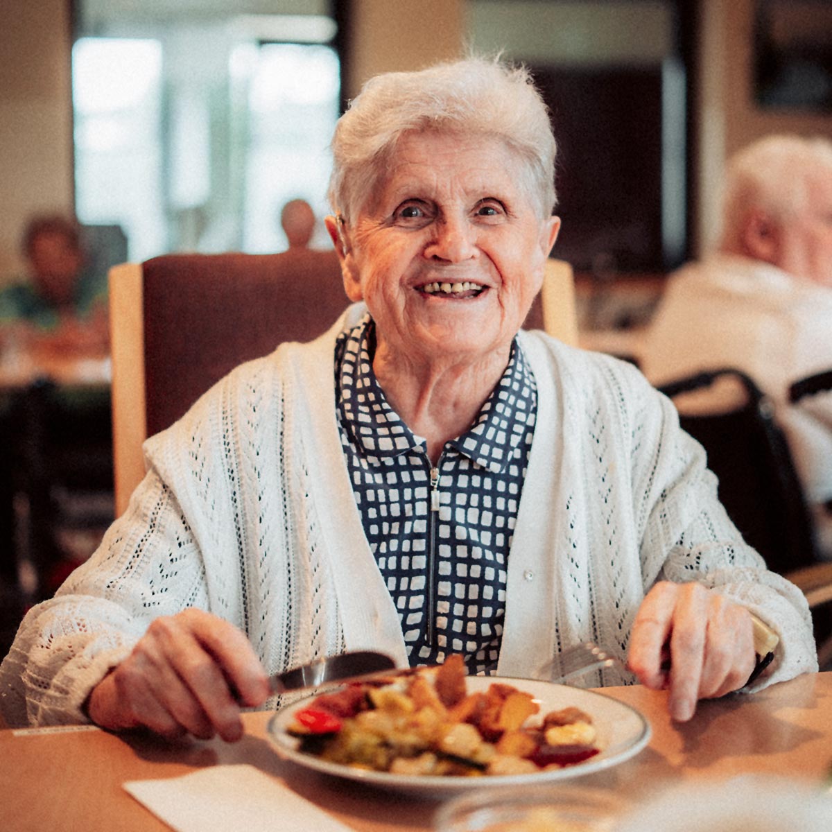 Eine Bewohnerin lächelt zufrieden beim Mittagessen