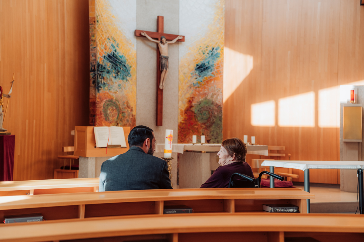 Der Pfarrer und eine Bewohnerin sitzen in der Bank der Kapelle