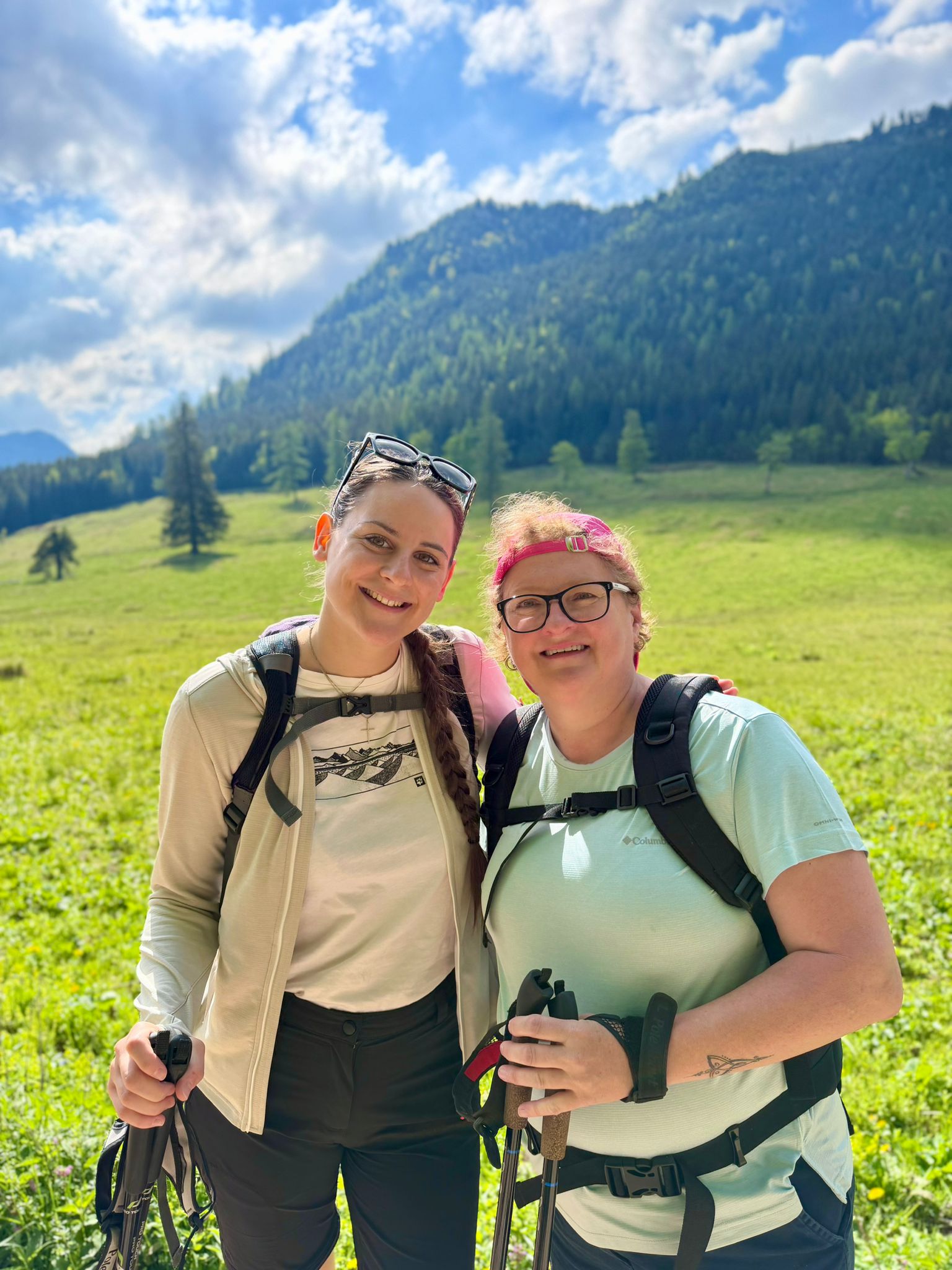 Zwei Mitarbeiterinnen fröhlich mit Wanderstöcken vor idyllischem Bergpanorama