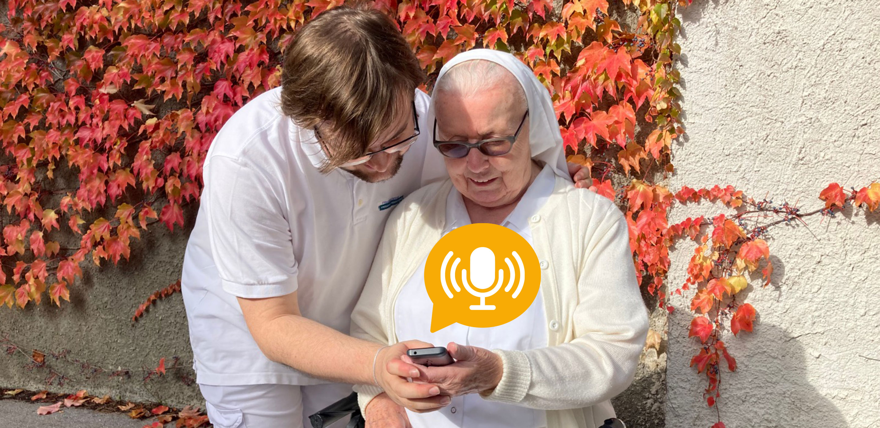 Pflegelehrling Benjamin zeigt einer Ordensschwester den neuen Podcast am Handy
