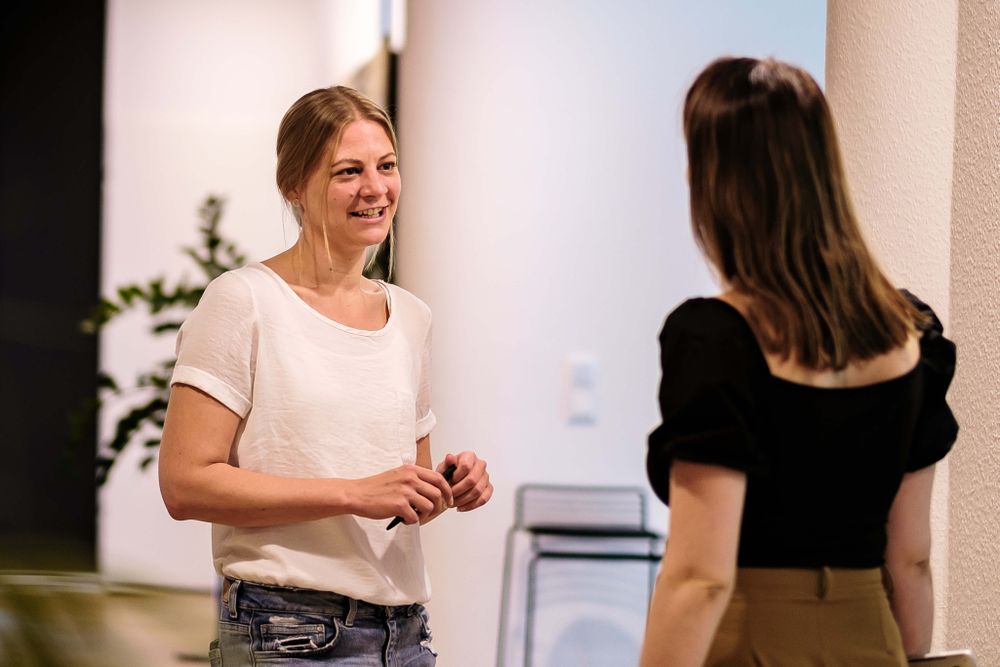 Zwei Frauen im Gespräch in einem Büroflur.