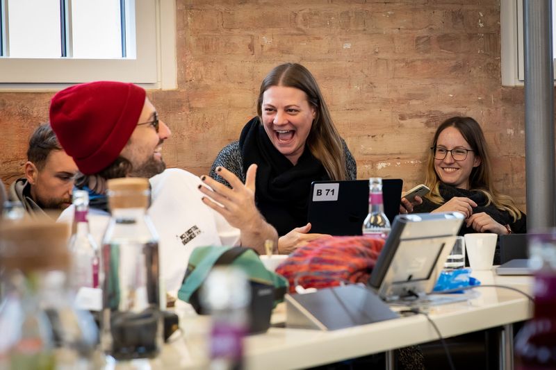 Fröhliche Teamarbeit mit lachenden Personen und Laptops.