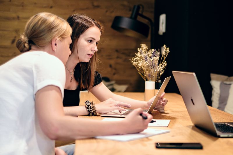 Zwei Frauen arbeiten mit Laptop und Notizen in gemütlicher Atmosphäre.