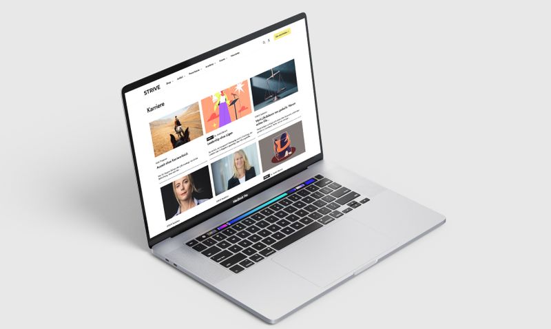 Open laptop displaying a vibrant website with articles and images, on a white surface against a light gray background.