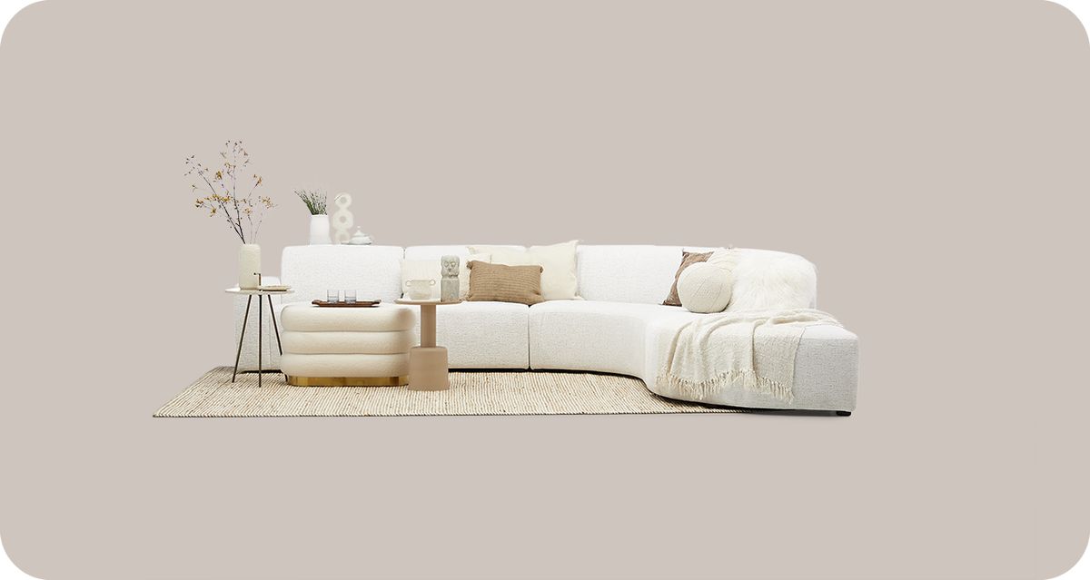 Witte modulaire bank met beige kussens en een deken, naast een bijzettafel met decoratieve elementen op een lichte achtergrond.