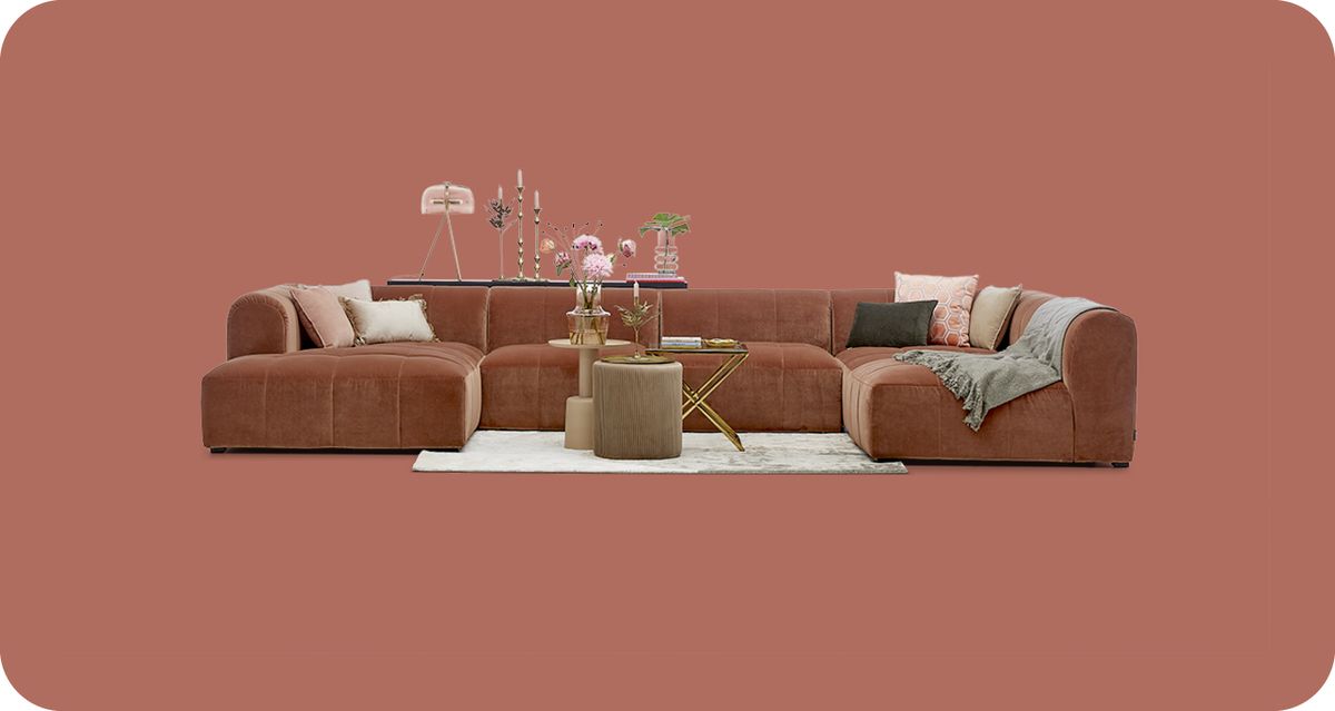 Grote, modulaire bruine bank met kussens, tafels, decoratieve objecten en een vloerkleed tegen een effen achtergrond.