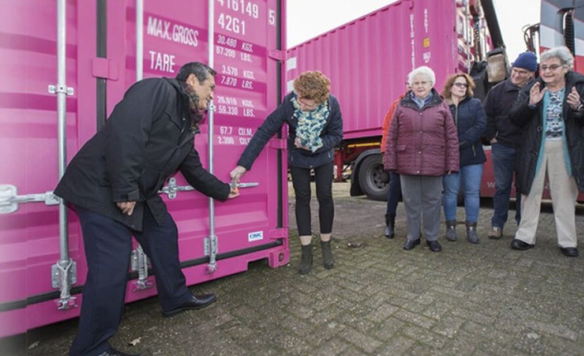 Een groep mensen opent een roze container. Een man en een vrouw zijn bezig het slot los te maken. Anderen kijken toe.