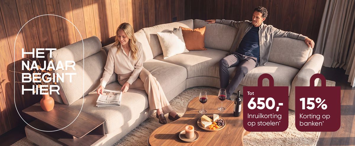 A woman and a man relax on a modern beige sectional sofa in a warmly lit living room with a round wooden coffee table and autumn promotions displayed.