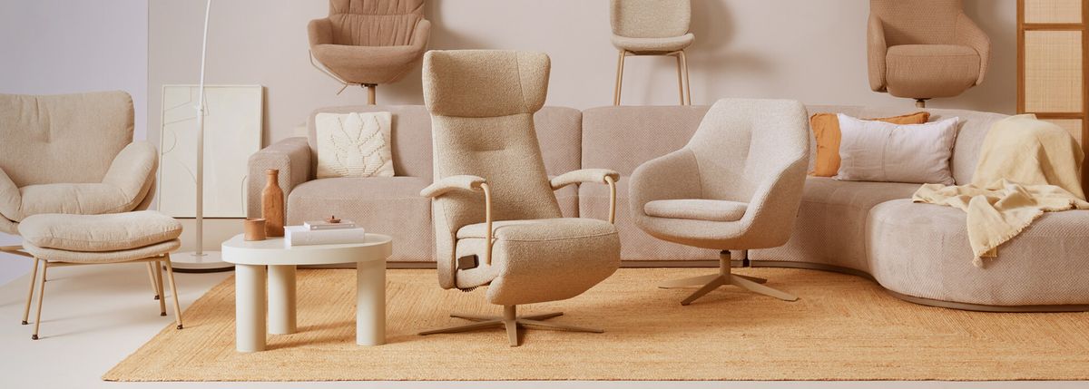 A cozy living room setup with beige armchairs, a comfortable sofa, round coffee table, decorative vases, and a soft rug on a light wooden floor.