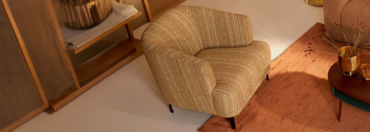 Cozy mustard-colored armchair with textured fabric, positioned on a warm-toned rug next to a stylish wooden side table with decorative plants.