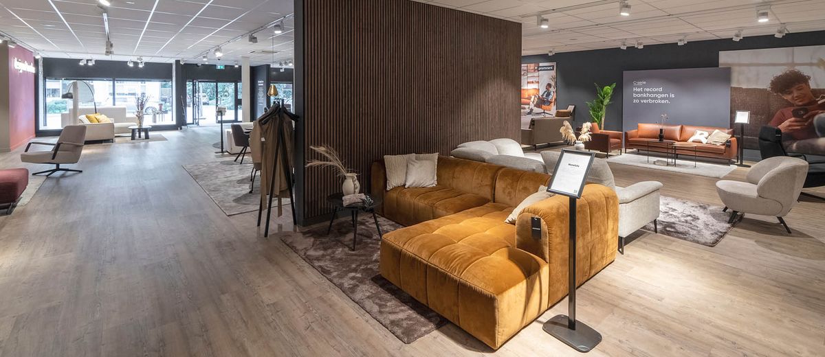 Moderne meubelshowroom met diverse zithoeken, waaronder een bruine fluwelen bank op een houten vloer, en zachte verlichting.