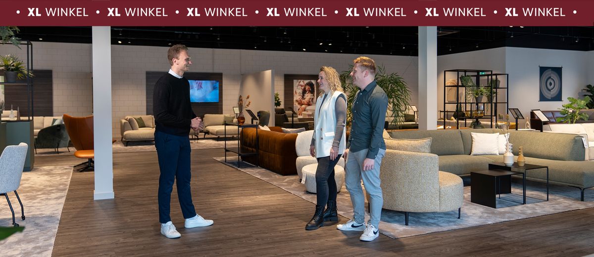 Drie mensen staan in een moderne meubelwinkel met banken en decoraties. Op de achtergrond zijn verschillende woonkamersets te zien.