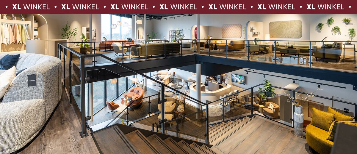 Interieur van een ruime meubelwinkel met moderne meubels verdeeld over twee verdiepingen, inclusief trappen en glazen balustrades.