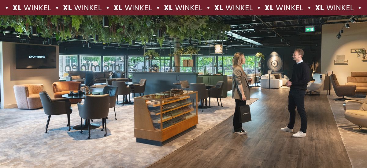 Moderne winkelinterieur met zitgedeelte, groene planten aan het plafond en twee mensen in gesprek.