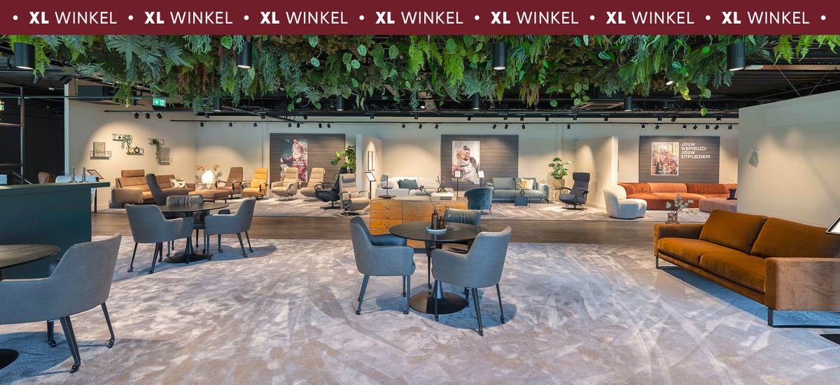 Moderne meubelwinkel met zitjes, tafels en banken, omringd door groene hangplanten aan het plafond, en diverse posters aan de muur.