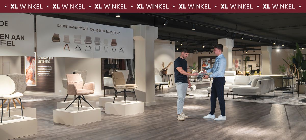 Twee mannen schudden handen in een stijlvolle meubelshowroom met moderne stoelen en banken.