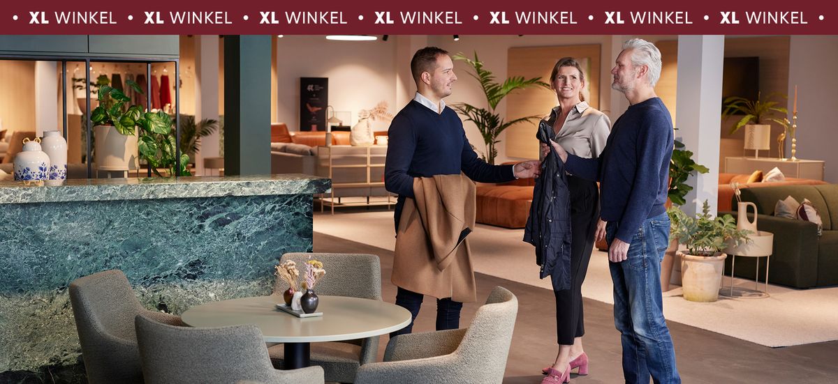 Drie mensen in gesprek in een moderne meubelwinkel. Ze staan naast een tafel met bloemen en planten, omringd door diverse zithoeken.