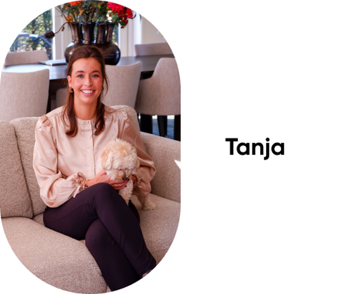 Vrouw glimlacht terwijl ze met een kleine witte hond op haar schoot op een beige bank zit. Achtergrond toont een woonkamer. Tekst: "Tanja".