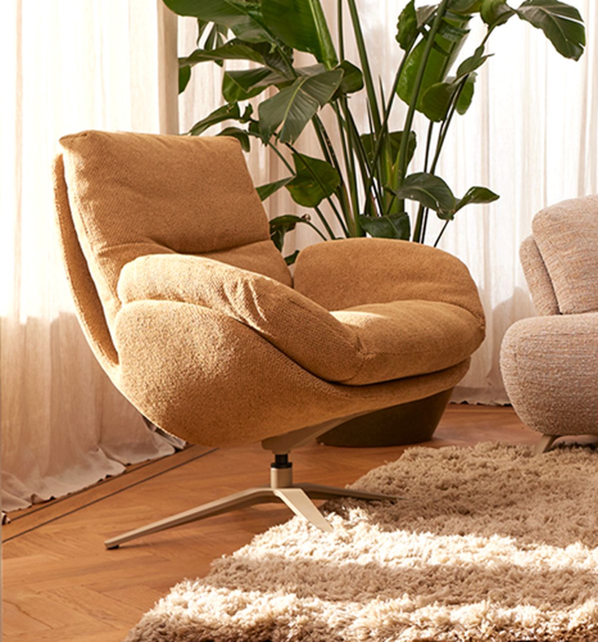 A cozy, tan swivel chair with plush cushions on a wooden floor, next to a shag rug and large plant, bathed in warm natural light.