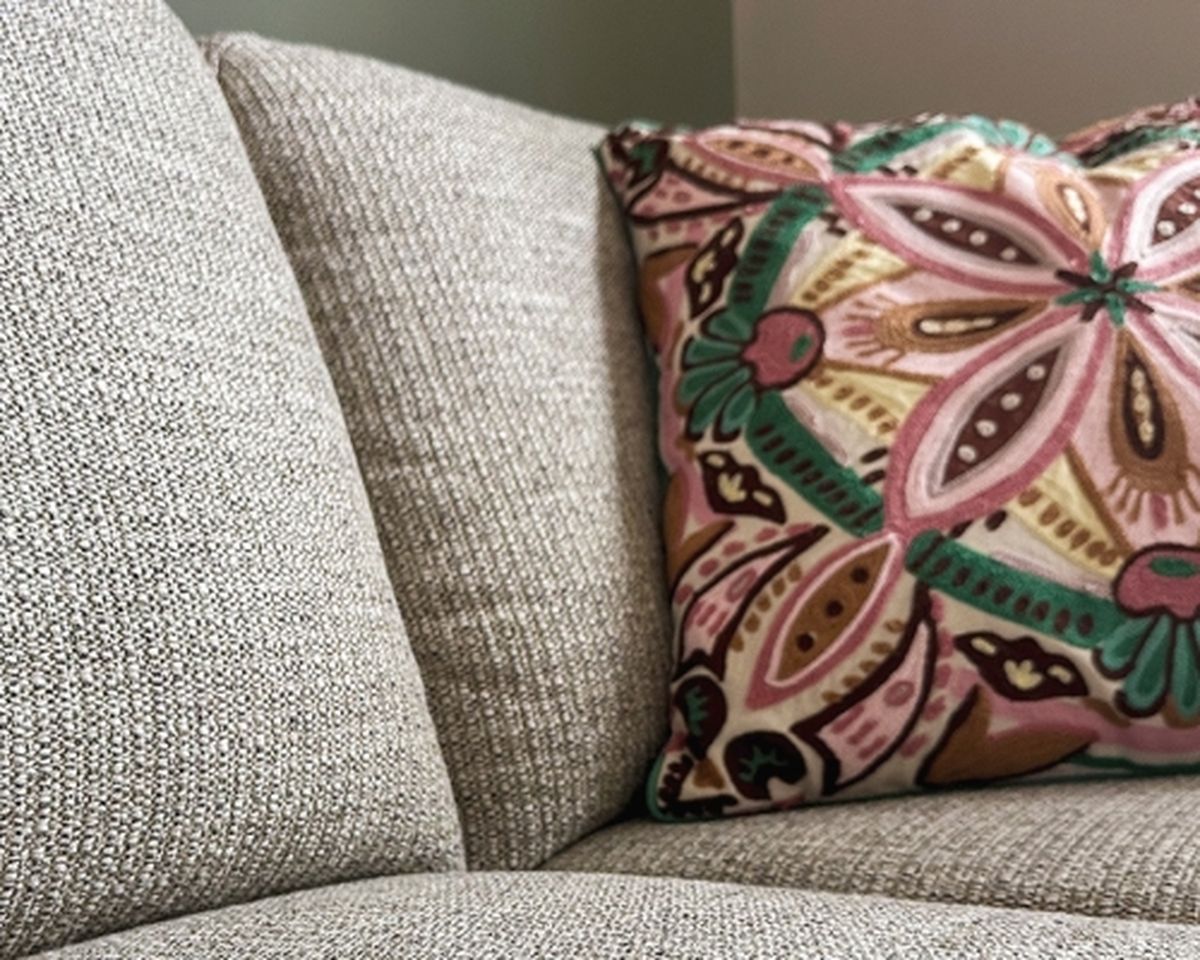 Gray textured sofa with a colorful pillow featuring a floral and geometric pattern in pink, green, and brown.