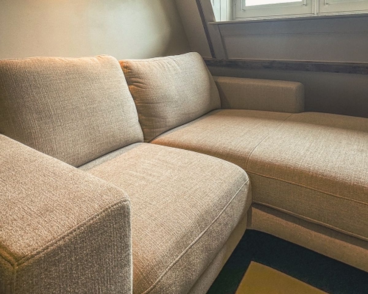 Beige fabric sectional sofa in a cozy corner with natural light from a nearby window, featuring a modern design and clean lines.