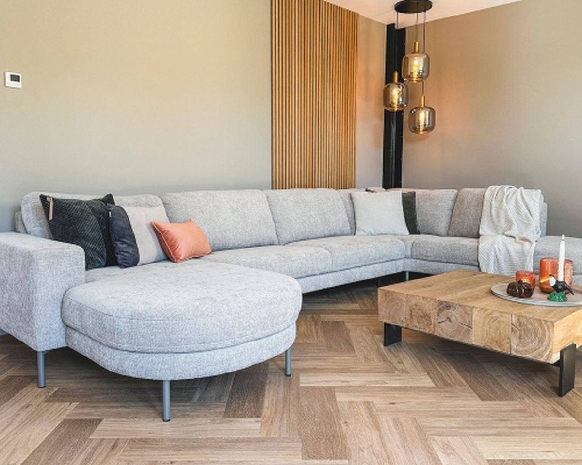 A modern living room with a light gray sectional sofa, wooden coffee table, black and gold pendant lights, and a cozy ambiance.