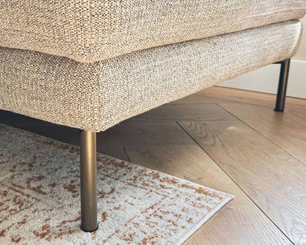 Beige textured sofa with metal legs on a wooden floor, partially over a patterned rug.