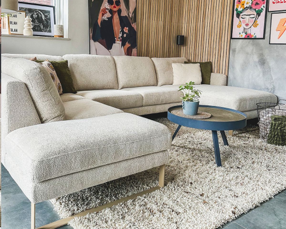 L-vormige beige sofa met kussens en een ronde tafel met plant.