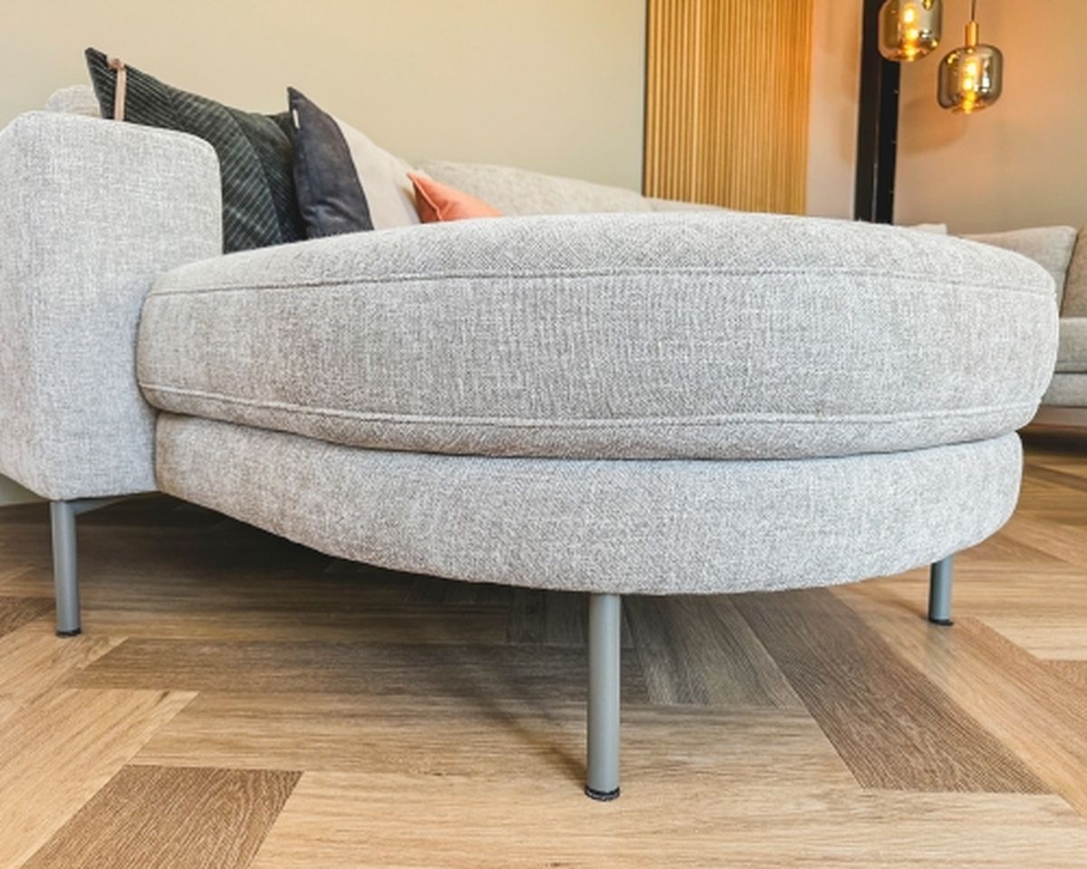 A modern gray sofa with a rounded edge and metal legs on a wooden parquet floor, complemented by decorative pillows.