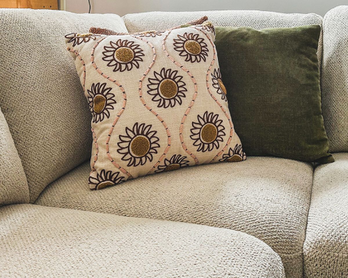 Een zachte, beige kussen met zonnebloemen en een groene velvet kussen op een bank.