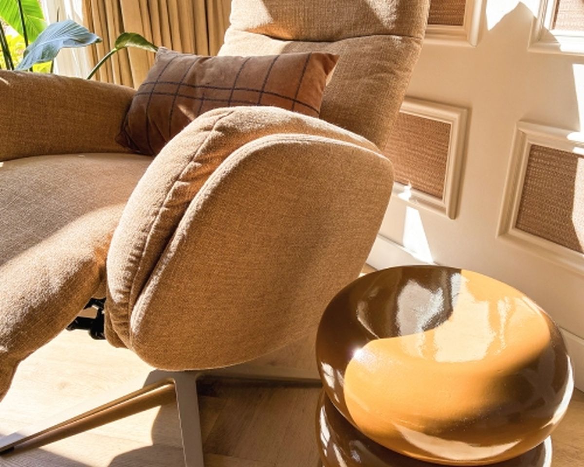 Cozy beige armchair with a plaid pillow beside a glossy brown round side table, basking in warm sunlight indoors.
