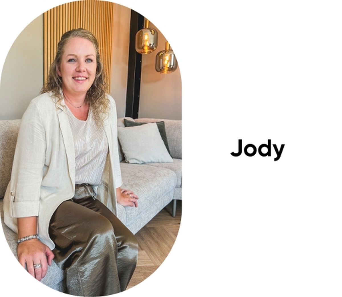 Woman with curly hair and a light-colored blouse and jacket sits on a couch, smiling. The word "Jody" is on the right.