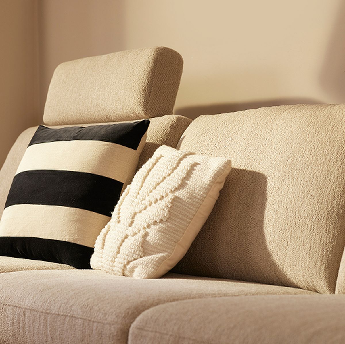 Beige sofa with a striped black and white pillow and a textured cream pillow, illuminated by warm, natural light.