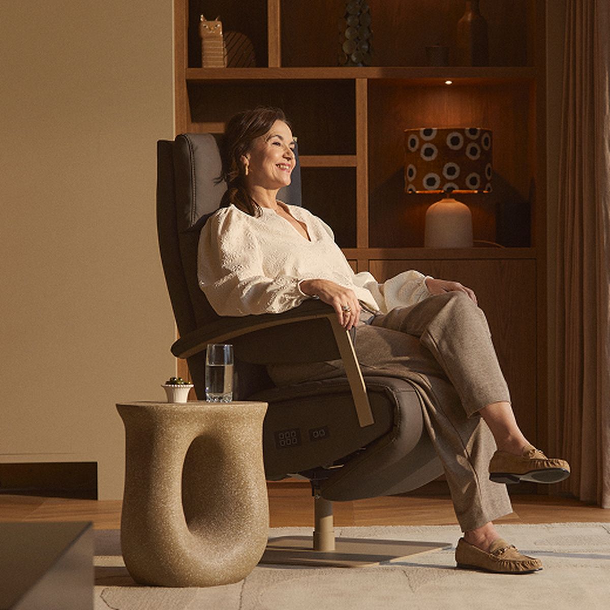 A woman relaxes in a comfortable armchair in a cozy living room, with a table holding a glass of water next to her.