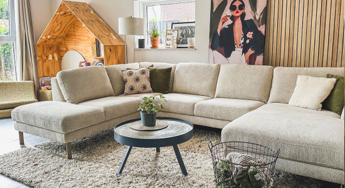 L-vormige beige sofa, bijzettafel, vloerkleed en een houten constructie.